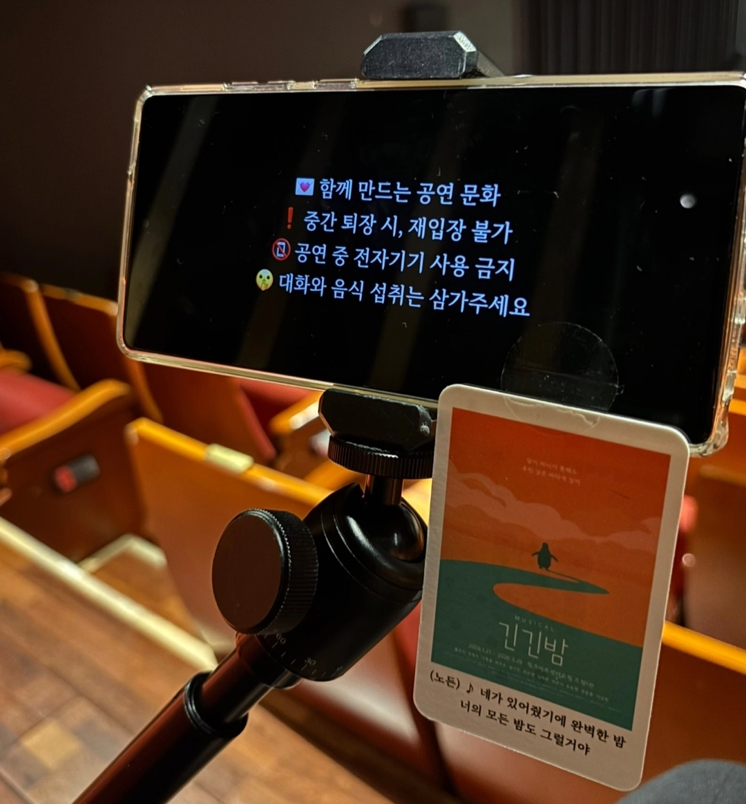 좌석 거치대 자막 단말기 화면 "함께 만드는 공연 문화 / 중간 퇴장 시, 재입장 불가 / 공연 중 전자기기 사용 금지 / 대화와 음식 섭취는 삼가주세요" + 거치대에 단 <긴긴밤> 포스터 카드(아래에 극중 가사 한 줄, 저작권 가사라 전사 생략)